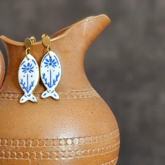 Boucles d’oreilles pendantes peintes a la main, en polymère incassables et légère, en forme de poisson motif bleu style vintage, présentés sur un pichet en terre cuite
